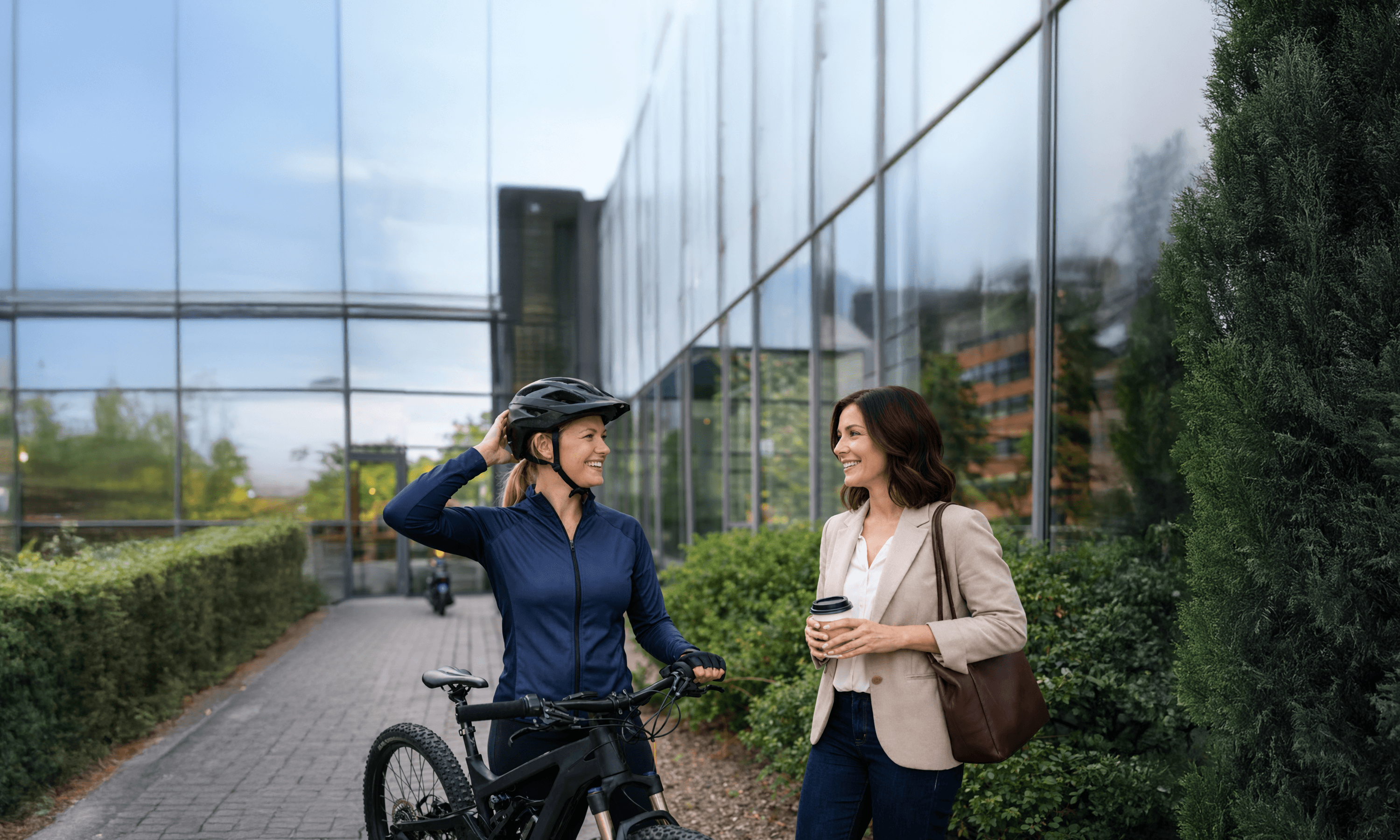 Työntekijä saapuu työpaikalle työsuhdepyörällä ja keskustelee kollegan kanssa toimistorakennuksen edessä.